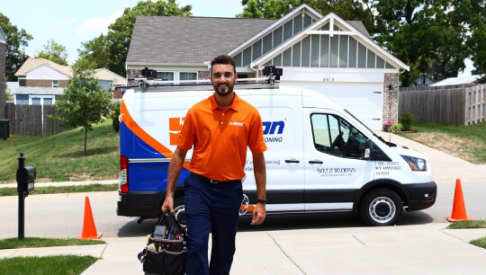 Airtron technician in uniform carrying tools by service van at residential home