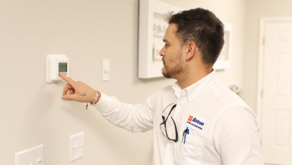 Airtron technician adjusting digital thermostat during air conditioning service