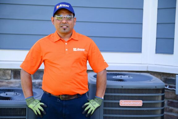 Airtron technician in orange uniform standing next to Goodman air conditioning units