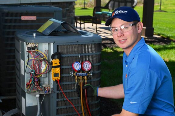 Airtron technician in blue uniform performing maintenance on Goodman air conditioning unit