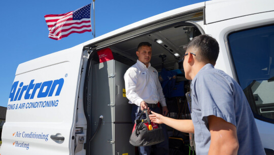 Airtron HVAC technicians at service van with American flag, discussing service call