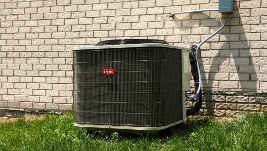 Bryant outdoor air conditioning unit installed on grass next to brick wall