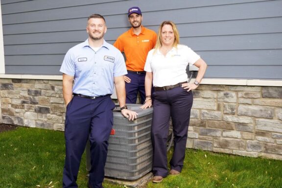 Airtron Indianapolis HVAC technicians standing next to an outdoor AC unit during a home visit