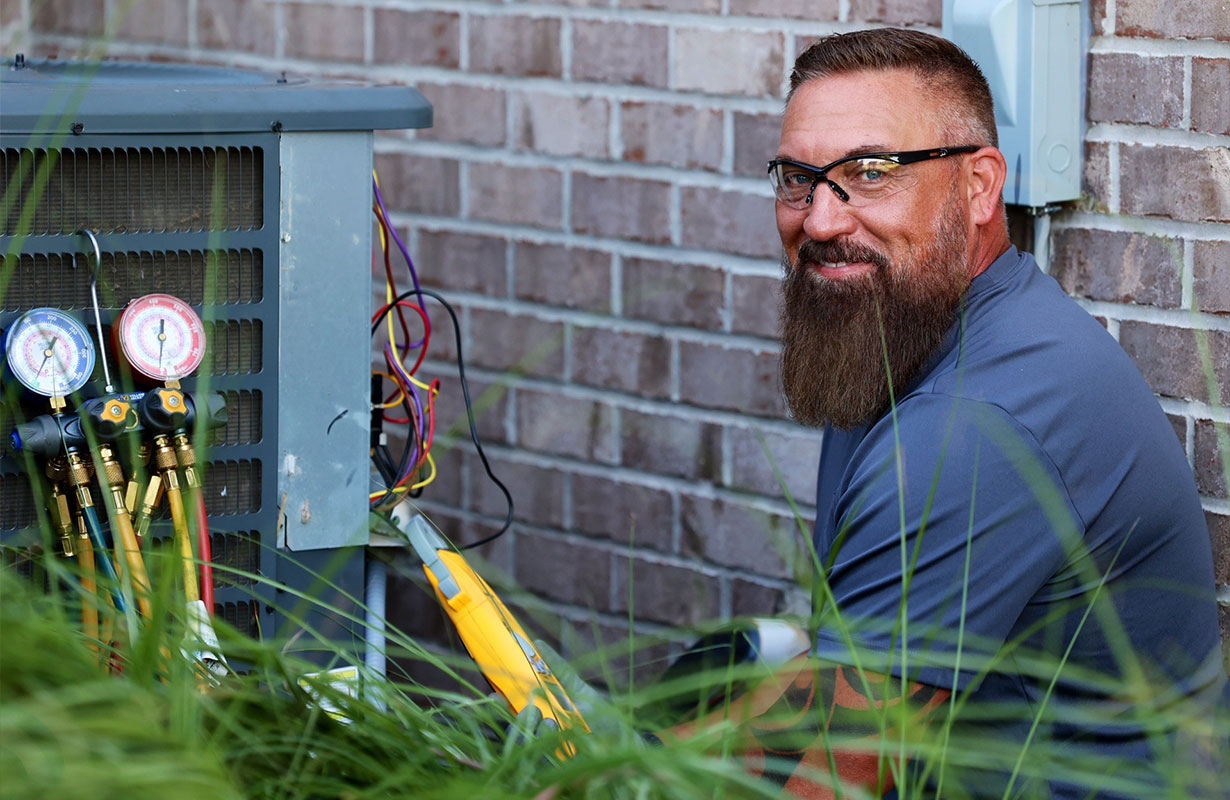 HVAC technician smiling in front of an outdoor AC unit while troubleshooting a repair